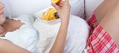 امرأة حامل مستلقية على الكنبة وتأكل برتقالة 