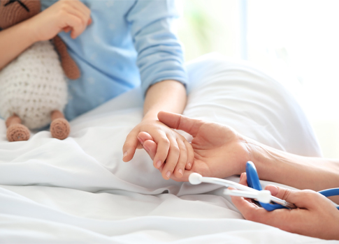 A pediatric patient holds the hand of a healthcare professional.