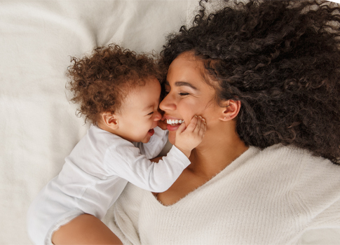 A mother is smiling as her young child holds her face.