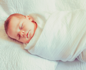 A swaddled baby sleeps on a white bed.