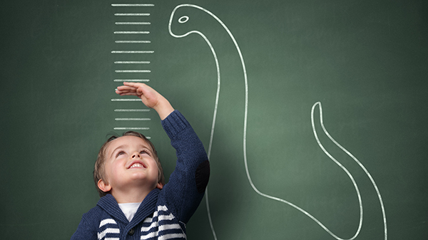 A child measuring his height against a dinosaur drawing.