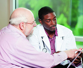 Male doctor looking at a tablet with an older male patient