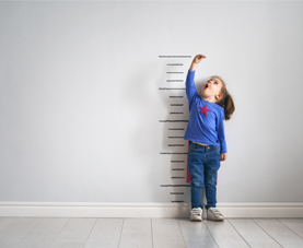 A young girl is standing against a wall to measure her height.