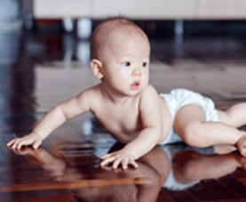 A diaper-clad baby crawls on a hardwood floor.