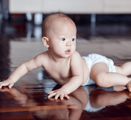 A diaper-clad baby crawls on a hardwood floor.