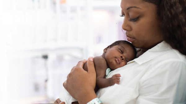 Nurse lovingly holds newborn baby against her chest.