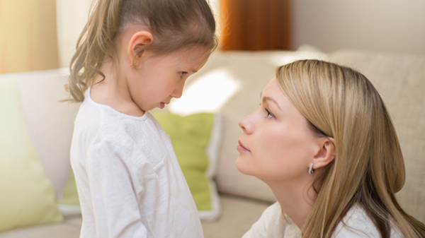 A mother kneels in front of her young daughter and looks her in the eye.