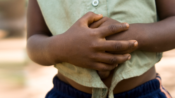 A young child has his hands clasped over his abdomen.
