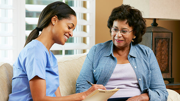 A nurse smiling and taking notes next to a middle-aged female patient