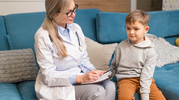 Doctor with clipboard sits on couch with young boy.