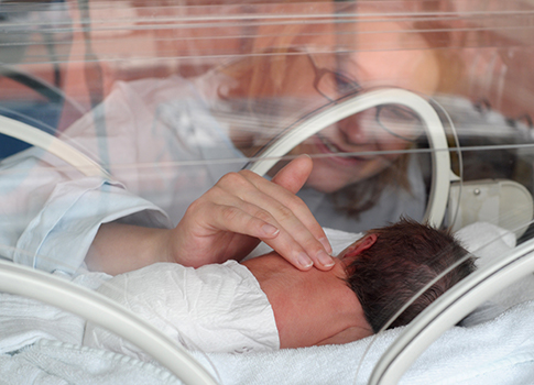 A woman patting the back of an infant baby inside the NICU
