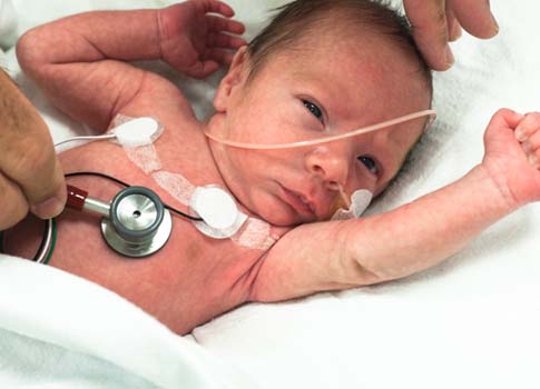 A healthcare practitioner examines a baby with a stethoscope.