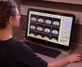 Technician sits before a computer monitor looking at CT scans