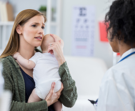 A lady holding a baby talking to a medical professional 