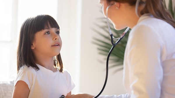 Pediatrician uses stethoscope to listen to little girl’s lungs a the child takes a deep breath