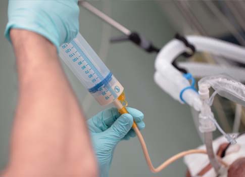 A healthcare provider’s hands push a syringe into a tube.