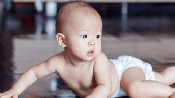 A diaper-clad baby crawls on a hardwood floor.