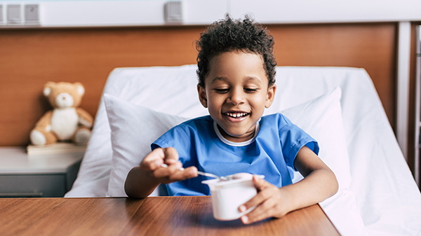 A little boy eating a cup of yogurt on the hospital bed