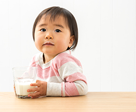A baby sitting by a table and holding a glass of milk