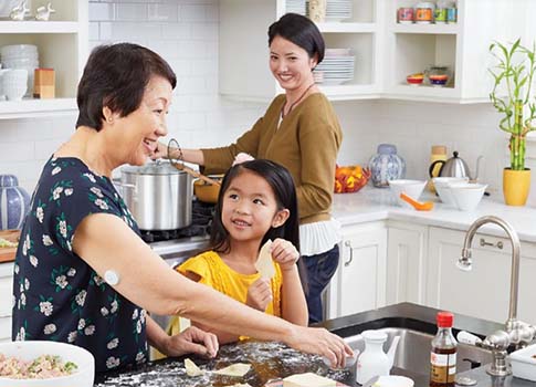 A multi-generational family prepares a meal in a home kitchen.