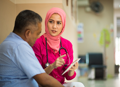 A nurse talking to a middle-aged male patient and pointing at her charts