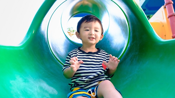 A little boy goes down a tube slide at a park