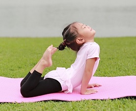 A little girl does yoga in the park on a pink yoga mat