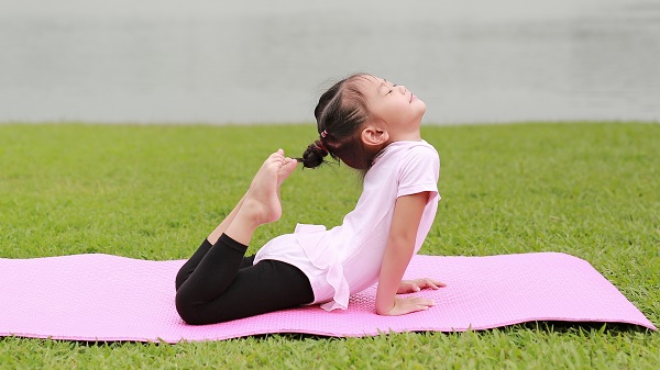 A little girl does yoga in the park on a pink yoga mat