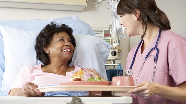 Nurse smiles while bringing food tray to hospitalized patient