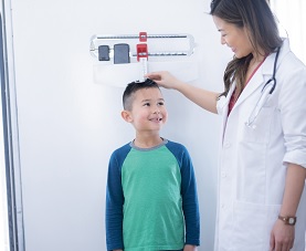 A nurse measures a little boy's height as he stands on an upright scale