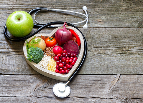 Fruits, vegetables, and grains in a heart-shaped bowl next to a stethoscope