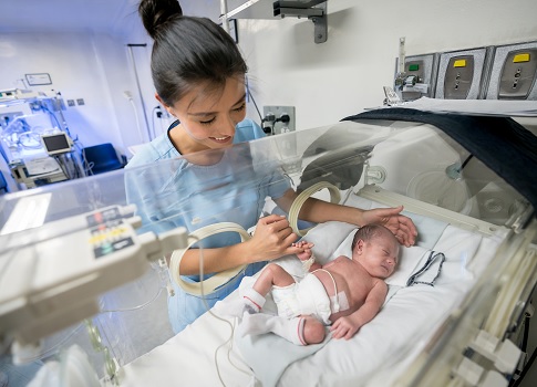 Recién nacido prematuro dentro de una incubadora sosteniendo el dedo de una enfermera que sonríe