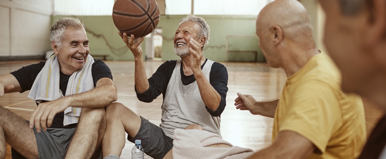 Group of older guys sit on gymnasium floor after playing basketball