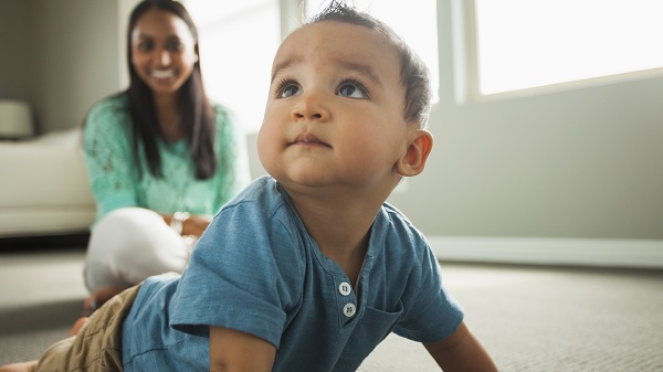 Smiling mother watches her child crawl across the floor