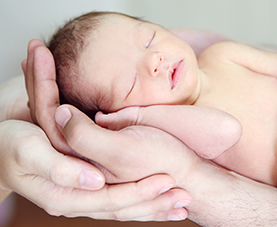 An infant baby sleeping on an adult's hands