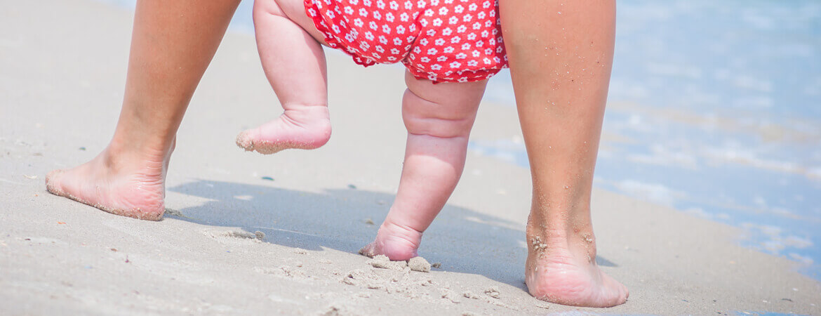 أقدام أم وطفلها يسيران على شاطئ البحر