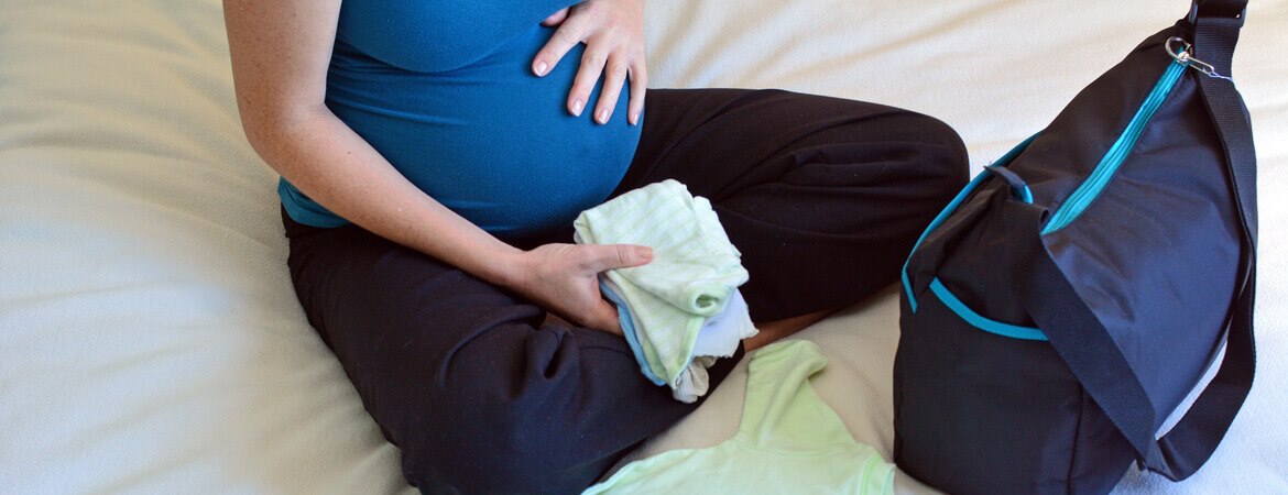 امرأة حامل تجلس على السرير وتحضر حقيبة الولادة