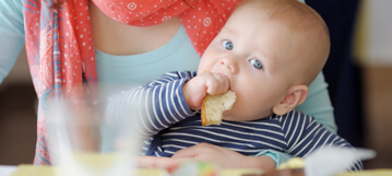 صورة طفل يجلس في حضن والدته ويتناول الخبز