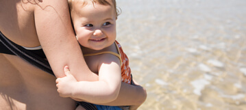 طفل يبتسم بين ذراعي والدته في البحر