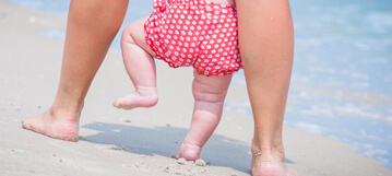أقدام أم وطفلها يسيران على شاطئ البحر