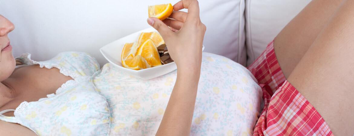 امرأة حامل مستلقية على الكنبة وتأكل برتقالة
