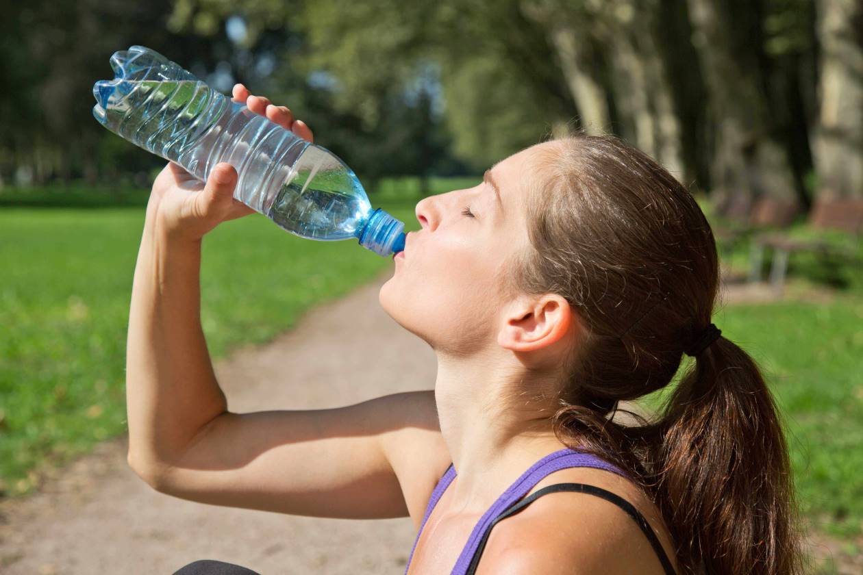 امرأة شابة رياضية تشرب الماء من القنينة