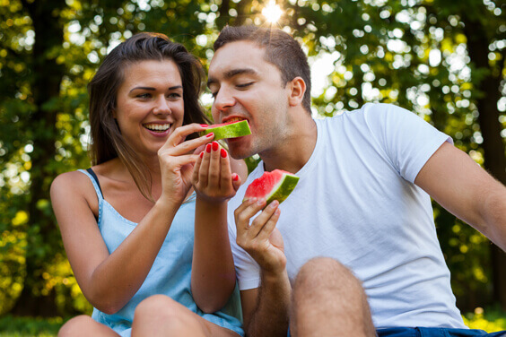 زوجان شابان يجلسان على العشب ويأكلان البطيخ