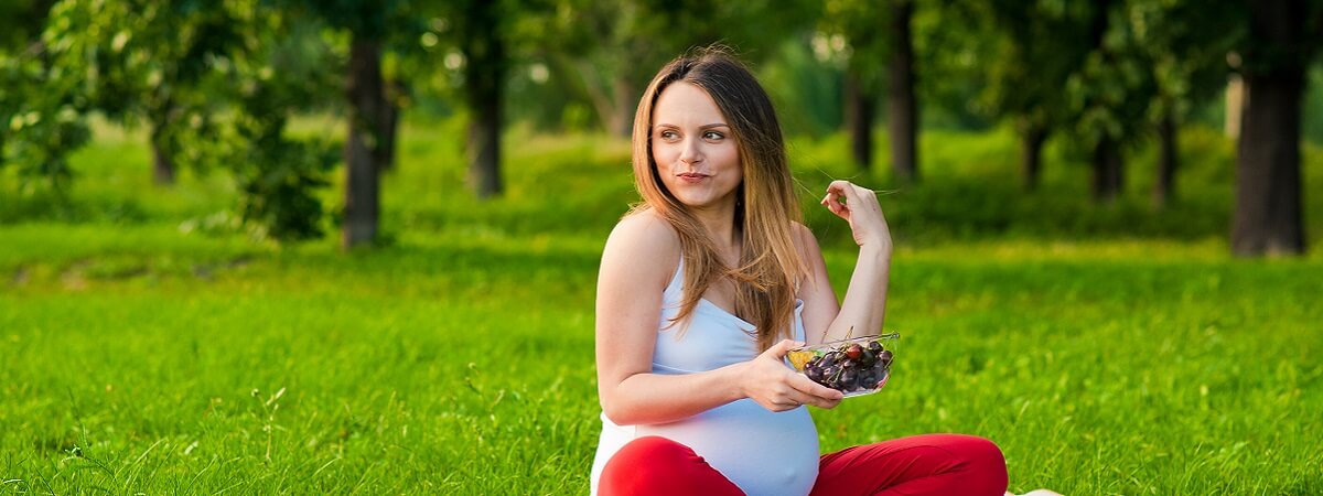 امرأة حامل تجلس في حديقة وتأكل من صحن فاكهة
