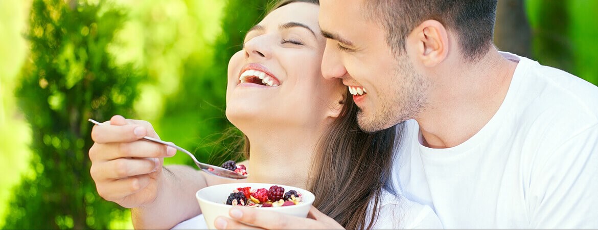 شاب مبتسم يجلس مع زوجته في الحديقة ويطعمها فاكهة برية