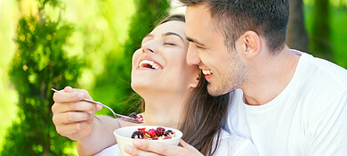 شاب مبتسم يجلس مع زوجته في الحديقة ويطعمها فاكهة برية