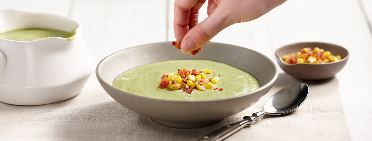 Avocado soup made with Ensure® Regular garnished with corn and bacon
