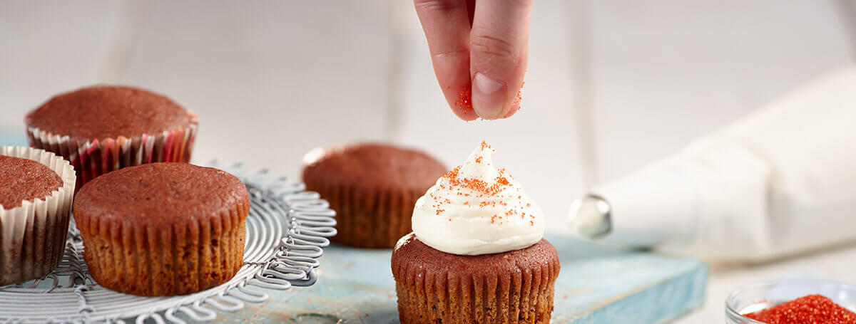 Adding sprinkles to moist red velvet cupcakes made with Ensure®
