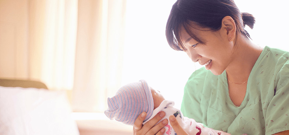 An Asian mother holding onto her newborn infant in a room