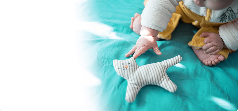 Infant learning to move body by reaching for a plush toy on bed 
